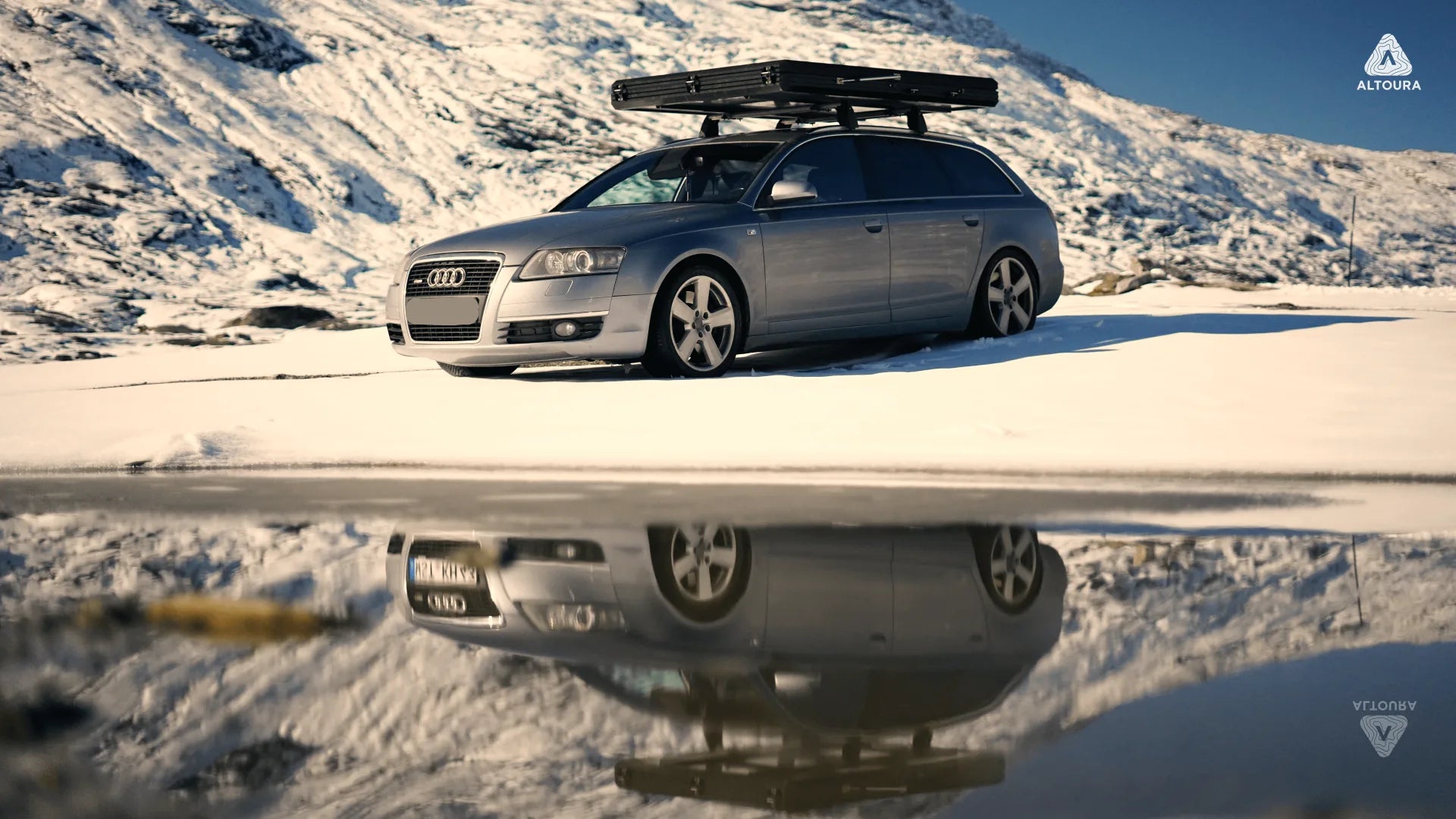 Audi Kombi mit Altoura Dachzelt in verschneiter Berglandschaft mit Spiegelung